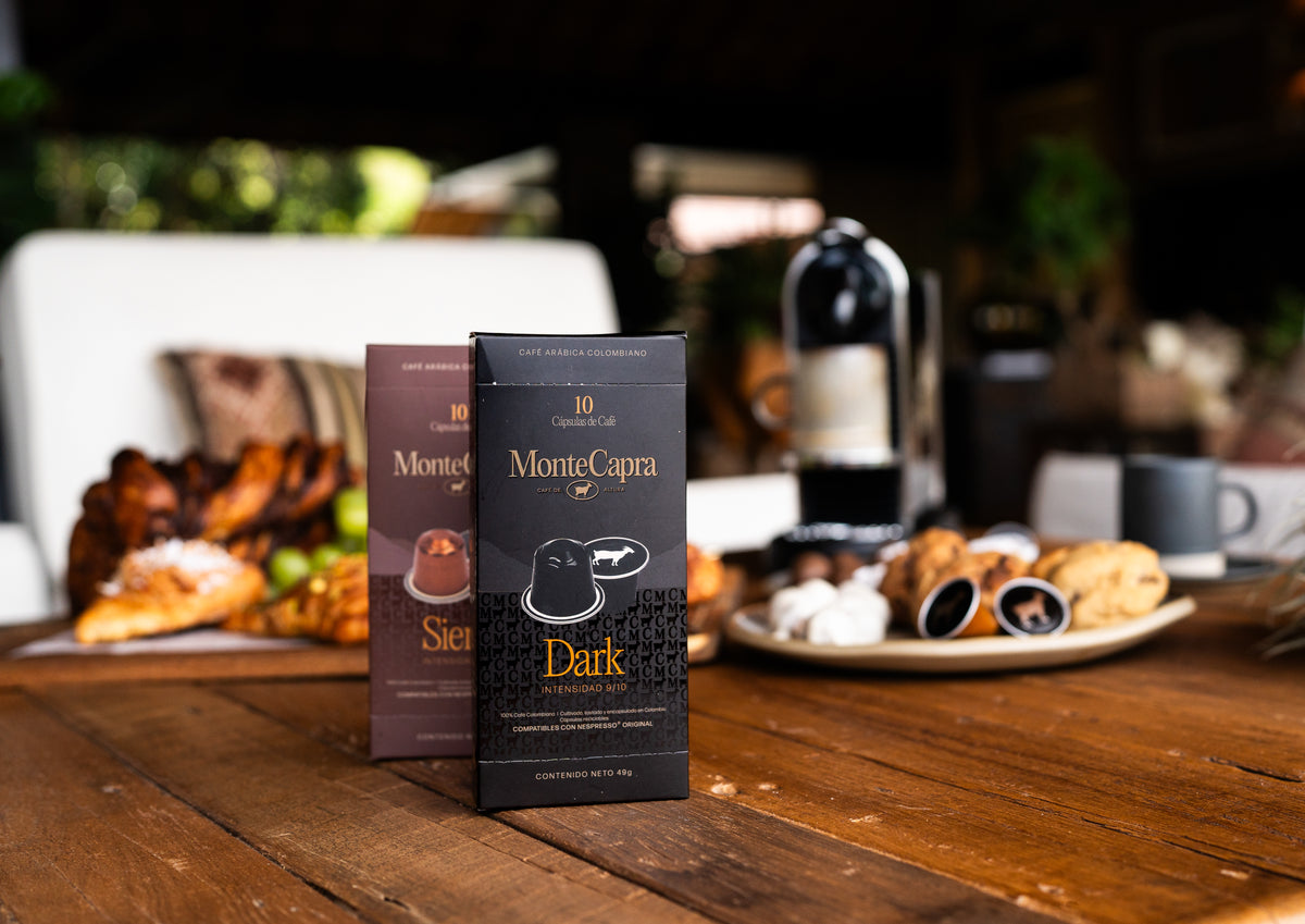 Cajas de cápsulas Monte Capra Siena y Dark sobre una mesa de madera junto a una cafetera y pasabocas